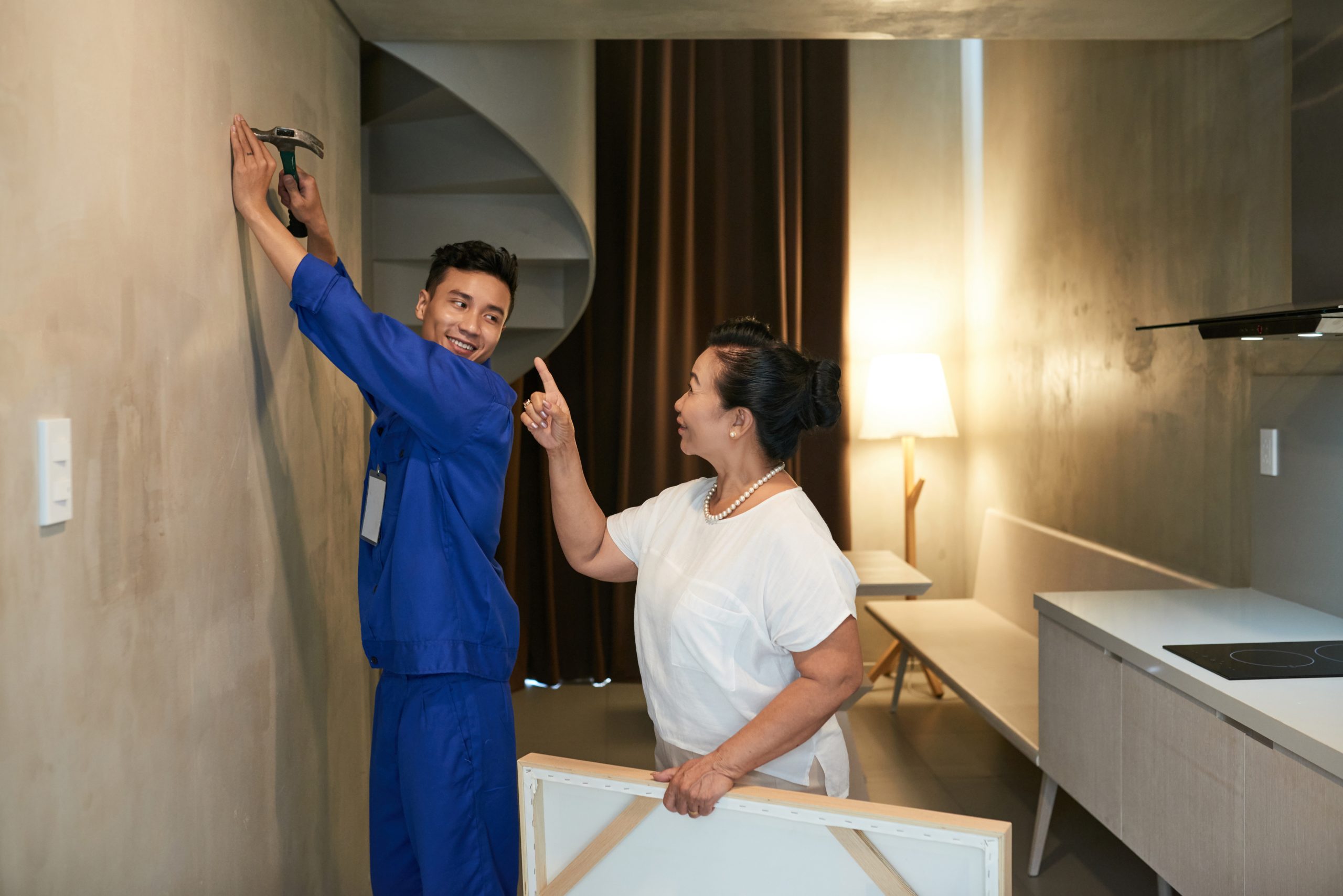 Cheerful young handyman helping senior woman to hang a picture